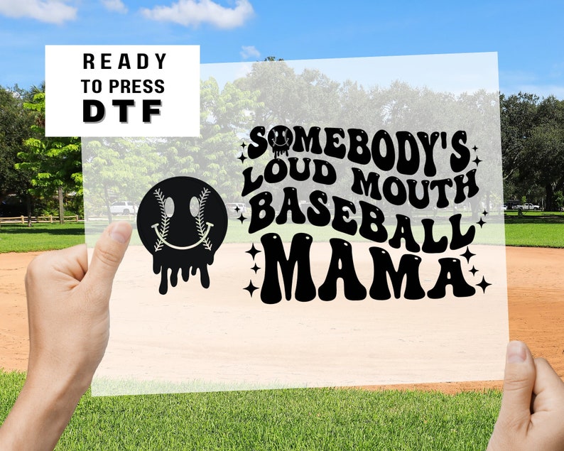 May include: A black and white design on a clear sheet, featuring a smiley face with baseball stitches for eyes, dripping down, and the text "Somebody's Loud Mouth Baseball Mama" in a retro font.