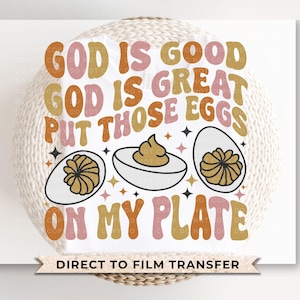 May include: A white iron-on transfer with the text "God is good, God is great, put those eggs on my plate" in pink, orange, and brown lettering. The text is surrounded by small stars and three cartoon eggs with yolks.