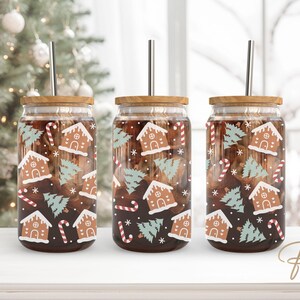Op de afbeelding: Drie glazen glazen met bruine deksels en roestvrijstalen rietjes. De glazen zijn versierd met een kerst gingerbread house en boompatroon.