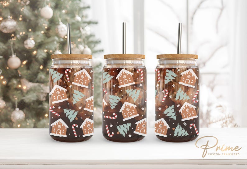 Op de afbeelding: Drie glazen glazen met bruine deksels en roestvrijstalen rietjes. De glazen zijn versierd met een kerst gingerbread house en boompatroon.