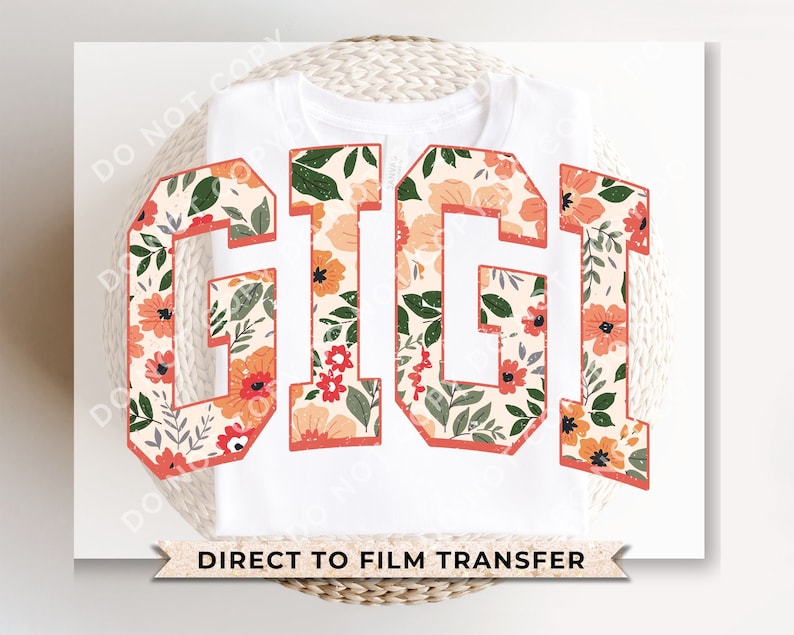 May include: White t-shirt with the word "GIGI" in large, bold letters. The letters are filled with a floral pattern featuring orange, pink, and green flowers. The text "DIRECT TO FILM TRANSFER" is printed below the letters.