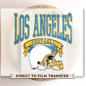May include: A white t-shirt with a blue and yellow graphic design featuring the text "Los Angeles Football" and a football helmet. The text "Direct to Film Transfer" is printed at the bottom of the shirt.