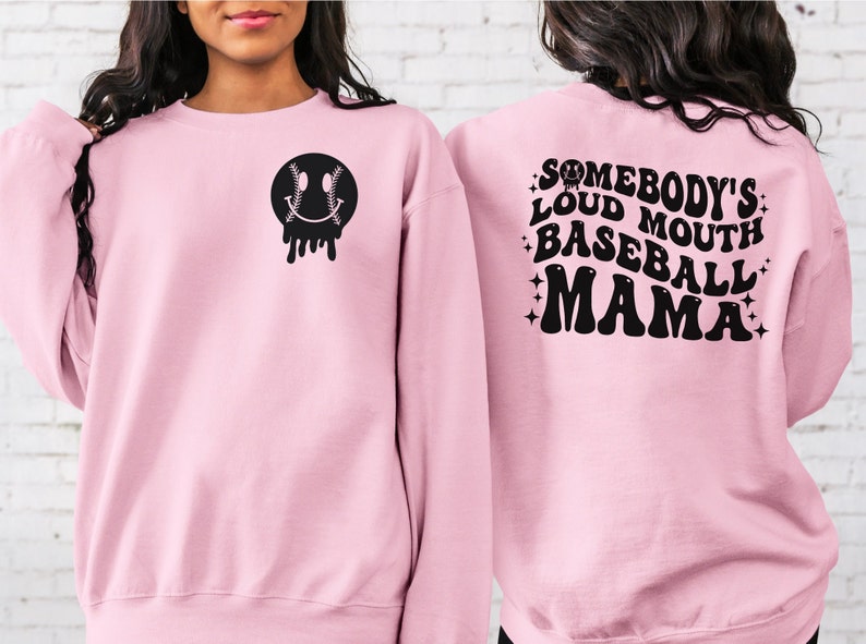 May include: Pink sweatshirt with a black baseball-themed smiley face on the front and the text "Somebody's Loud Mouth Baseball Mama" on the back.