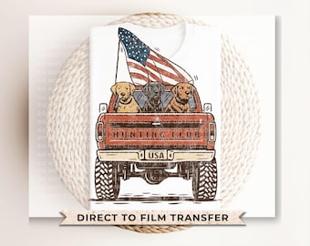 May include: White t-shirt featuring a red pickup truck with three dogs and an American flag. The truck has the text "HUNTING CLUB" and a "USA" license plate. The image also includes the text "DIRECT TO FILM TRANSFER".