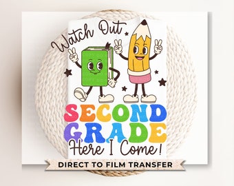 May include: A white t-shirt featuring a graphic of a green book and a yellow pencil with arms and legs making peace signs. The text reads Watch Out, SECOND GRADE, and Here I Come! in colorful, wavy, and script fonts with small black stars.