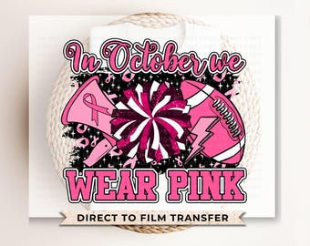 May include: Pink and black graphic design with a football, megaphone, and a cheerleading pom-pom. The text reads "In October we wear pink" and "Direct to Film Transfer".