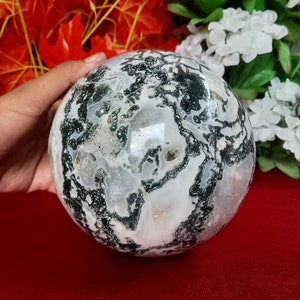 Può includere: Una sfera di agata bianca e verde con un motivo a spirale. La sfera è liscia e lucidata.