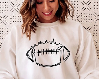 Puede incluir: Sudadera blanca con un contorno negro de un balón de fútbol y el texto "game day" en la parte delantera.