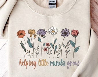May include: A beige sweatshirt with a floral design and the text "helping little minds grow".
