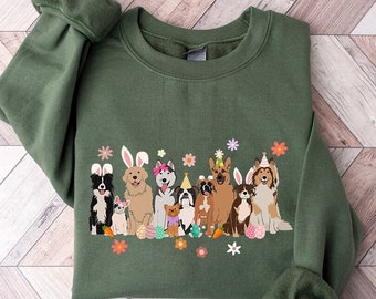 May include: A dark green sweatshirt featuring a graphic of various dog breeds, each adorned with Easter-themed accessories like bunny ears and party hats. Colorful Easter eggs and flowers are also included in the design. The sweatshirt has long sleeves.