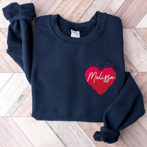 May include: A navy blue sweatshirt with a red heart made of smaller hearts. The heart has the name "Melissa" written inside it.