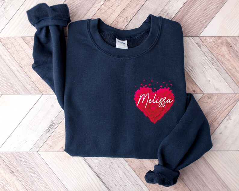 May include: A navy blue sweatshirt with a red heart made of smaller hearts. The heart has the name "Melissa" written inside it.