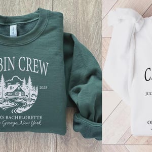 May include: A forest green sweatshirt and a white sweatshirt, each featuring a graphic of a cabin in the woods with the text CABIN CREW, JULY 2025, OLIVIA'S BACHELORETTE, and Lake George, New York. The forest green shirt has white text, while the white shirt has black text.