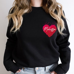 May include: Black sweatshirt with a pink heart design and the name "Melissa" written in white inside the heart.