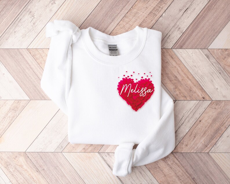 May include: White sweatshirt with a pink heart made of smaller hearts. The heart has the name "Melissa" written inside.