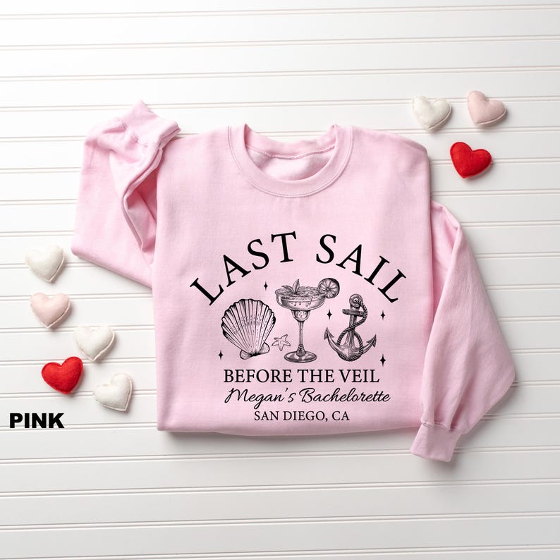 May include: Pink sweatshirt with the text "LAST SAIL BEFORE THE VEIL" and a seashell, cocktail, and anchor graphic. The text "Megan's Bachelorette" and "San Diego, CA" are also printed on the shirt.
