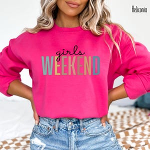 Peut inclure: Un sweat-shirt rose avec le texte "girls weekend" en couleurs arc-en-ciel.