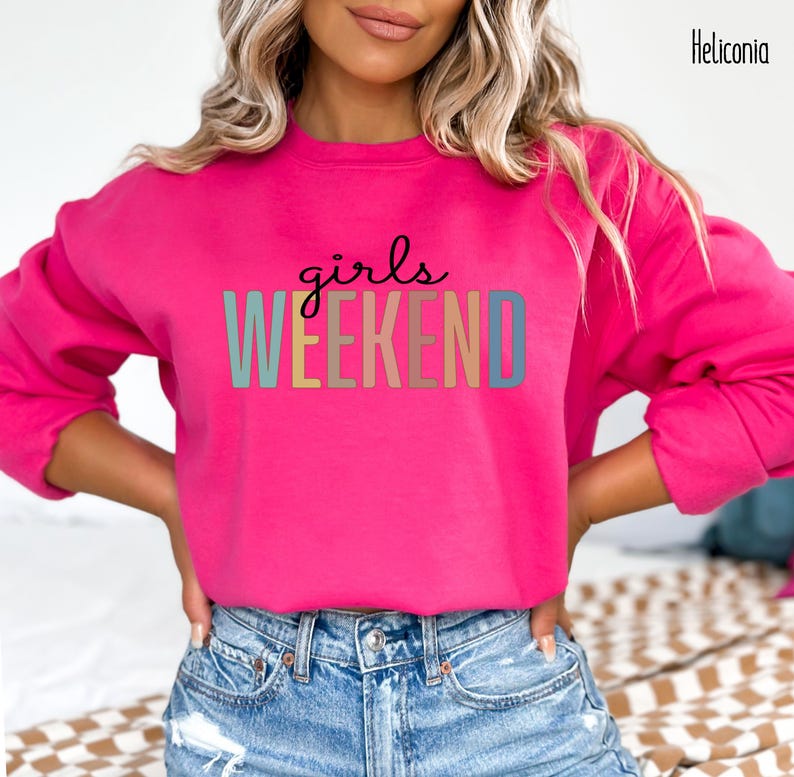 Peut inclure: Un sweat-shirt rose avec le texte "girls weekend" en couleurs arc-en-ciel.