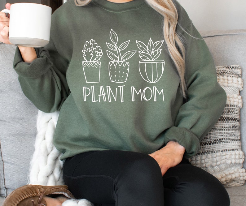 May include: A green sweatshirt with a white graphic of three potted plants and the text "PLANT MOM".