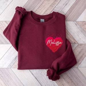 May include: Burgundy sweatshirt with a pink heart design and the name "Melissa" printed inside the heart.