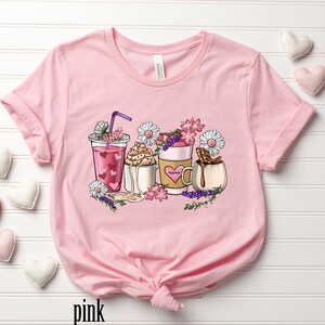 Pode incluir: Camiseta rosa com um gr&aacute;fico de cinco bebidas de caf&eacute; diferentes com flores e a palavra "mama" em uma das x&iacute;caras.