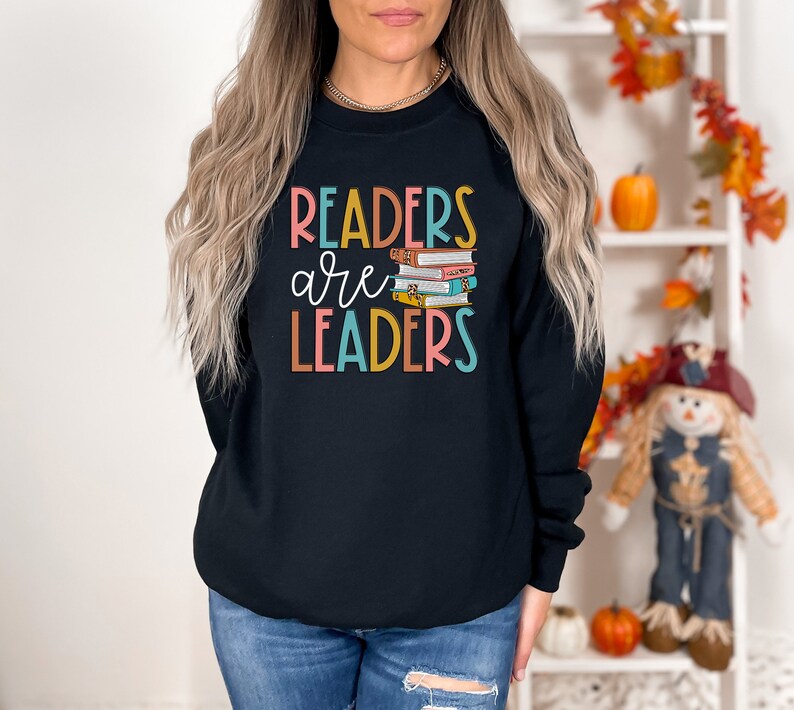 May include: Black sweatshirt with the text "Readers are Leaders" in colorful letters. A stack of colorful books is pictured next to the text.