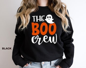 May include: A black long-sleeve sweatshirt featuring the white text THE, the orange text BOO, and the white text crew. A small white ghost graphic is positioned next to the word THE. The word BLACK is printed in the bottom left corner.