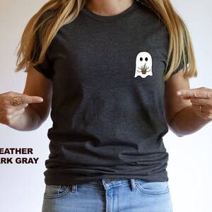 Puede incluir: Una camiseta gris oscuro jaspeada con un fantasma blanco que sostiene una taza de caf&eacute; helado marr&oacute;n. El texto "HEATHER DARK GRAY" est&aacute; impreso debajo de la imagen.