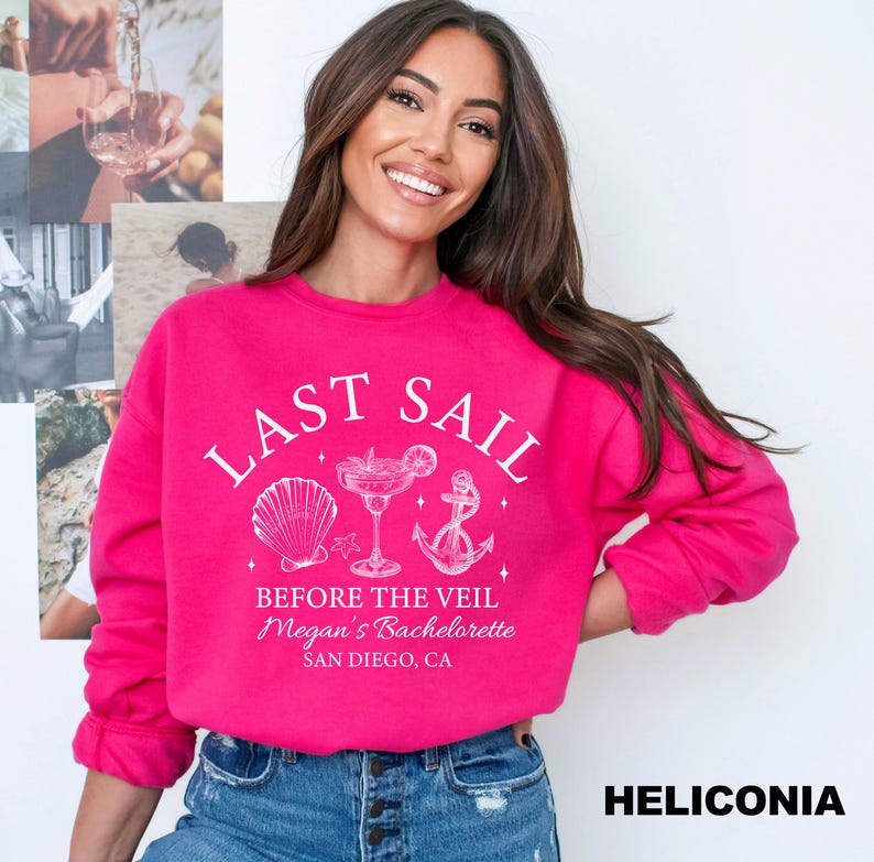 May include: A bright pink sweatshirt with the text "LAST SAIL" and "BEFORE THE VEIL Megan's Bachelorette SAN DIEGO, CA" in white. The design includes a seashell, cocktail, and anchor. The sweatshirt is a casual style.