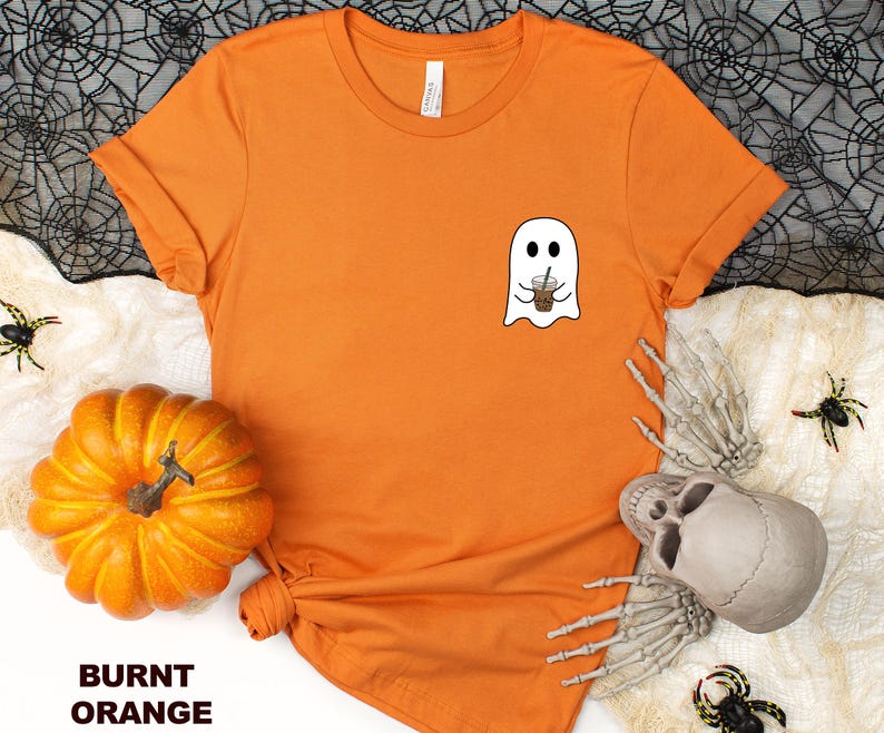 Puede incluir: Camiseta naranja quemada con un fantasma blanco sosteniendo una taza de caf&eacute;. El fantasma tiene una sonrisa amigable.