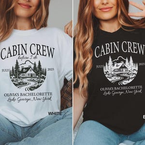 May include: A white or black t-shirt featuring the text CABIN CREW, before I do, JULY 2025, OLIVIA'S BACHELORETTE, and LAKE GEORGE, NEW YORK. The graphic depicts a cabin nestled among pine trees with a winding path leading to the front door.