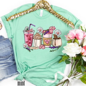 Pode incluir: Camiseta verde menta com um gr&aacute;fico de caf&eacute;, chocolate quente e um latte com flores e a palavra "morning" na x&iacute;cara de caf&eacute;.