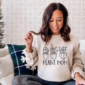 May include: A white sweatshirt with a black graphic of three potted plants and the text "PLANT MOM".