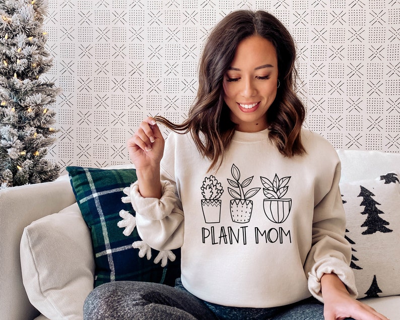 May include: A white sweatshirt with a black graphic of three potted plants and the text "PLANT MOM".