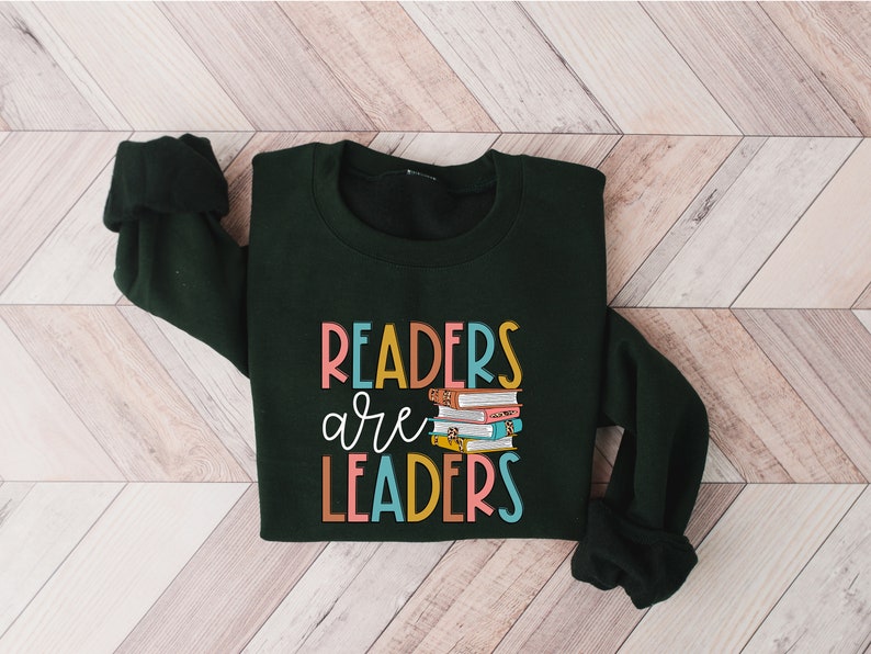 May include: A dark green sweatshirt with the text "Readers are Leaders" in colorful letters. A stack of colorful books is pictured next to the text.