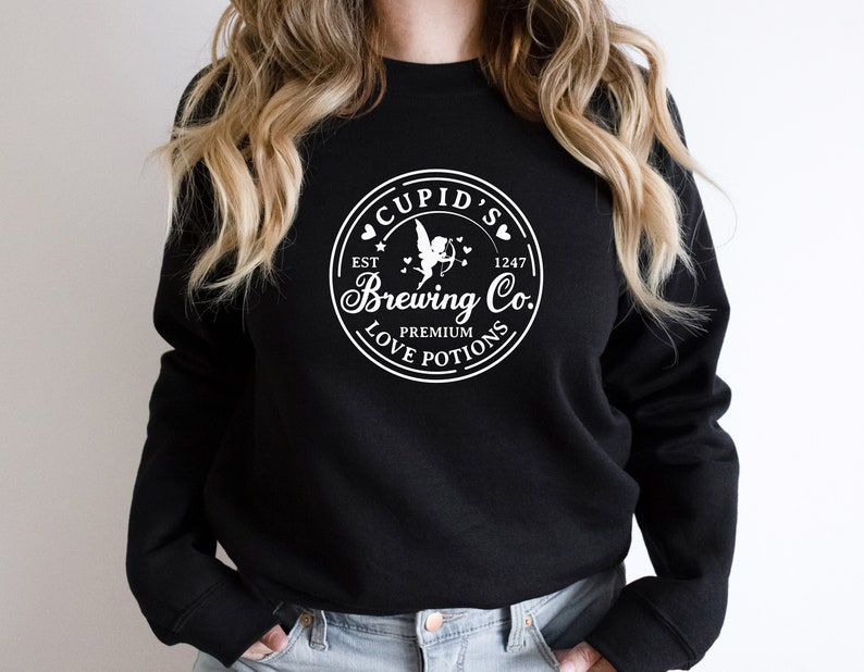 May include: Black sweatshirt with a white graphic of a circle with the text "Cupid's Brewing Co." inside. The graphic also includes a cupid with wings and arrows, hearts, and the text "Est 1247" and "Premium Love Potions".