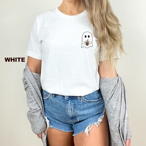 Puede incluir: Camiseta blanca con un fantasma sosteniendo una taza de caf&eacute;. El fantasma tiene dos ojos y una peque&ntilde;a sonrisa. El texto "WHITE" es visible en la esquina inferior izquierda de la imagen.