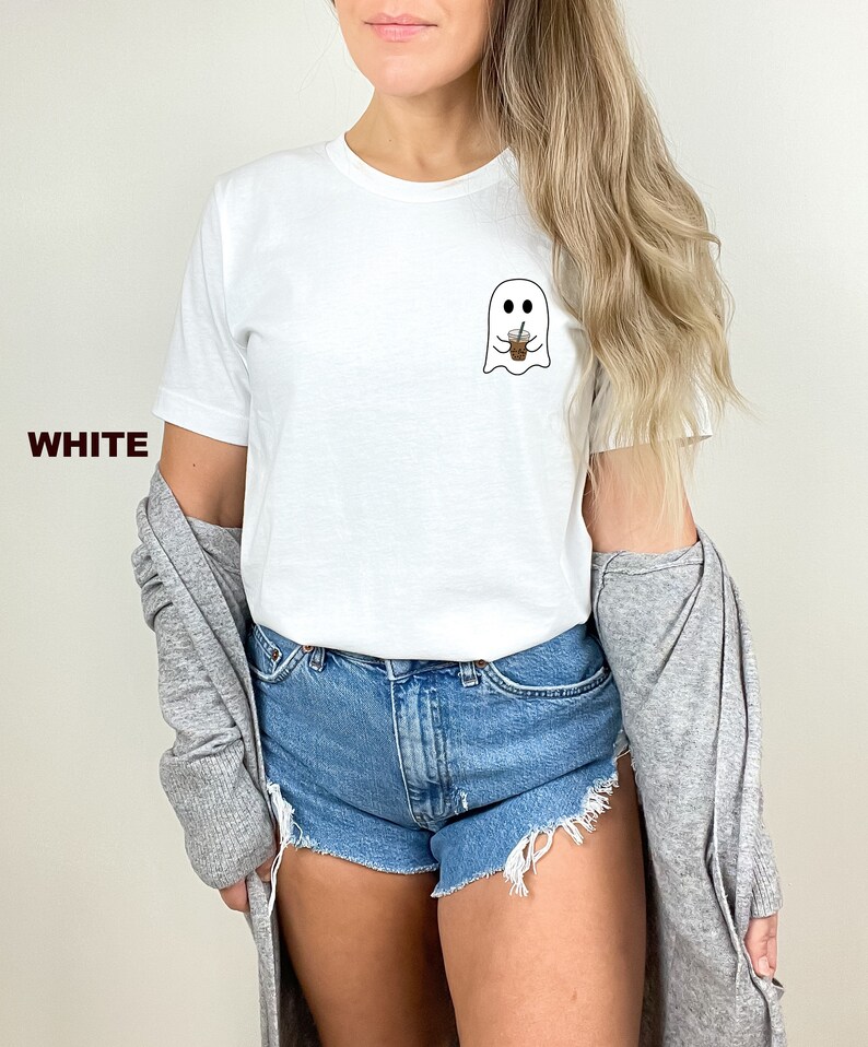 Puede incluir: Camiseta blanca con un fantasma sosteniendo una taza de caf&eacute;. El fantasma tiene dos ojos y una peque&ntilde;a sonrisa. El texto "WHITE" es visible en la esquina inferior izquierda de la imagen.