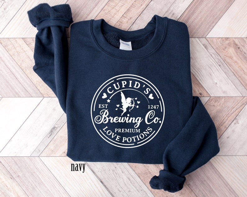 May include: Navy blue sweatshirt with a white graphic of a circle with the text "Cupid's Brewing Co." and a cupid with an arrow and hearts. The text "Est. 1247" and "Premium Love Potions" are also included in the graphic.