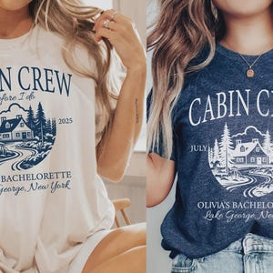 May include: Two short-sleeve t-shirts, one cream and one navy blue, featuring a circular graphic of a cabin in the woods with the text CABIN CREW, before I do, JULY 2025, OLIVIA'S BACHELORETTE, and Lake George, New York printed in a contrasting color.