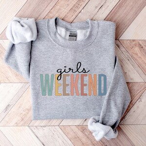 Peut inclure: Sweat-shirt gris avec le texte "girls weekend" en lettres color&eacute;es.