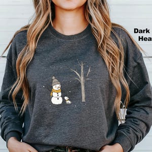 May include: A dark grey heather sweatshirt featuring a snowman and a small dog standing in front of a tree. The snowman is wearing a black hat and a yellow scarf. The dog is brown and white.