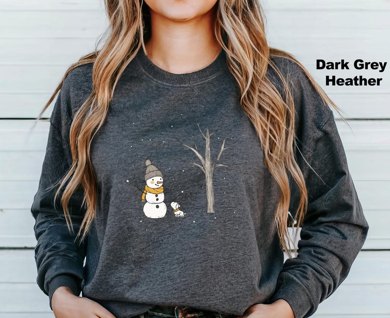 May include: A dark grey heather sweatshirt featuring a snowman and a small dog standing in front of a tree. The snowman is wearing a black hat and a yellow scarf. The dog is brown and white.
