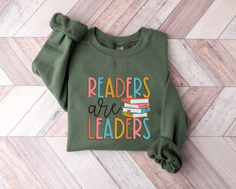 May include: A green sweatshirt with the text "Readers are Leaders" in colorful letters. A stack of books with colorful covers is pictured above the text.