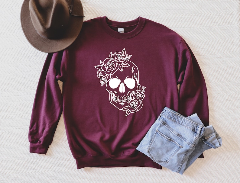 May include: A maroon sweatshirt with a white outline of a skull with flowers around it.