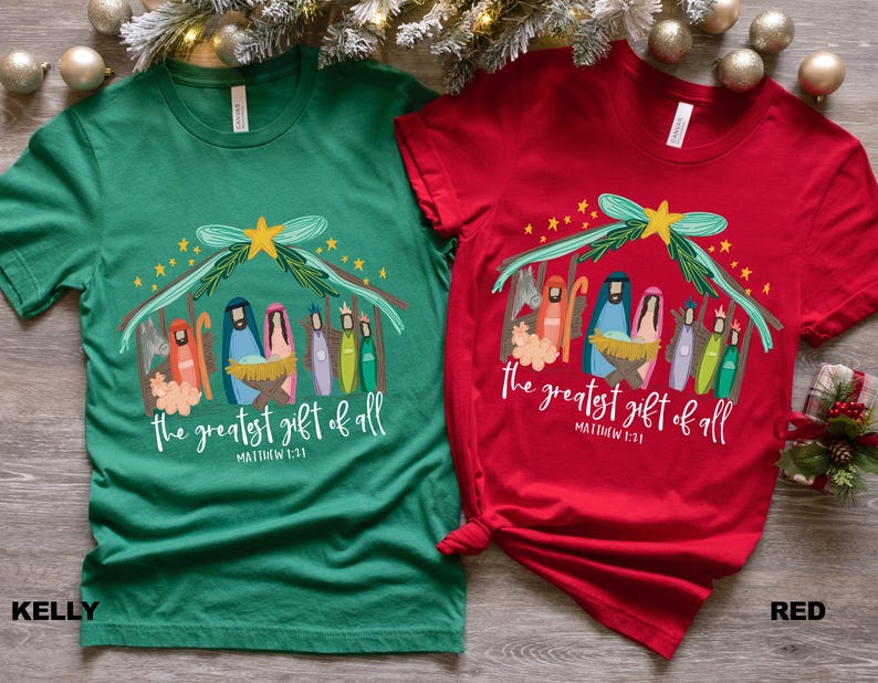 May include: Two t-shirts with a Christmas nativity scene design. The green shirt has the text "the greatest gift of all" and "Matthew 1:21". The red shirt has the text "the greatest gift of all" and "Matthew 1:21".