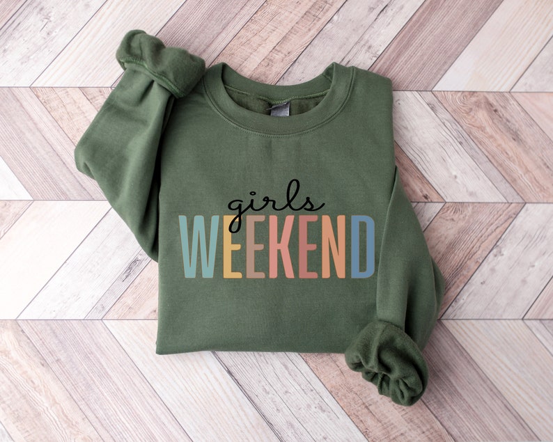Peut inclure: Un sweat-shirt vert avec le texte "girls weekend" en couleurs arc-en-ciel.