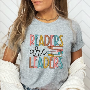 May include: A gray t-shirt with the text "Readers are Leaders" in colorful letters. A stack of books with a leopard print design is featured above the text.