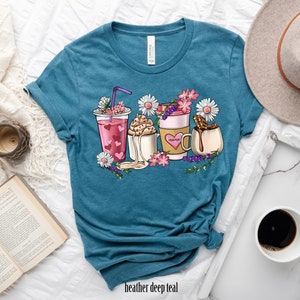 Pode incluir: Uma camiseta azul turquesa com um gr&aacute;fico de v&aacute;rias bebidas de caf&eacute; e ch&aacute; com flores e a palavra "Mama" em uma das x&iacute;caras.