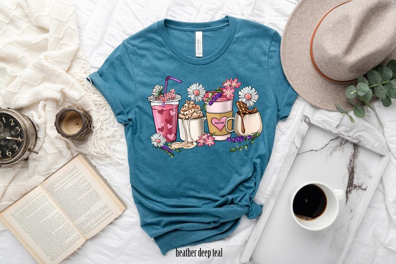 Pode incluir: Uma camiseta azul turquesa com um gr&aacute;fico de v&aacute;rias bebidas de caf&eacute; e ch&aacute; com flores e a palavra "Mama" em uma das x&iacute;caras.